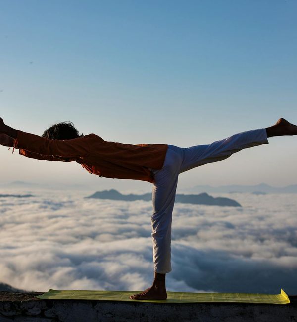 Silhouette of a person in a powerful yoga warrior pose at sunrise.